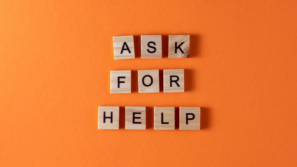 scrabble pieces spelling out ask for help on an orange background to depict a blog on asking for help in work and school