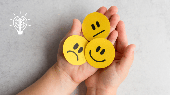 Hands holding three yellow emoji faces representing different emotions, symbolizing emotional awareness and understanding.