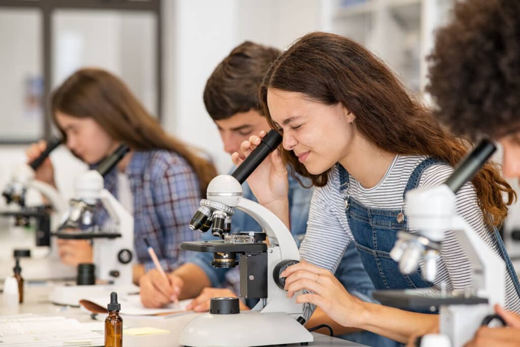 Group of high school students performing experiment using microscope in science lab.