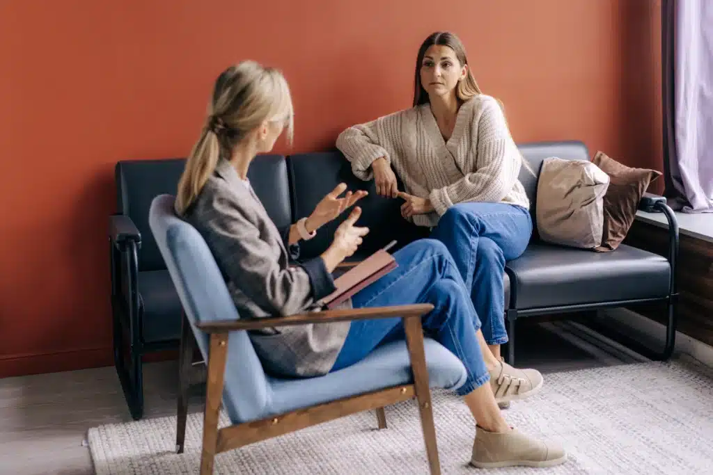 An ADHD coach facilitates a discussion with two clients on a sofa during a group coaching session in a comfortable office.