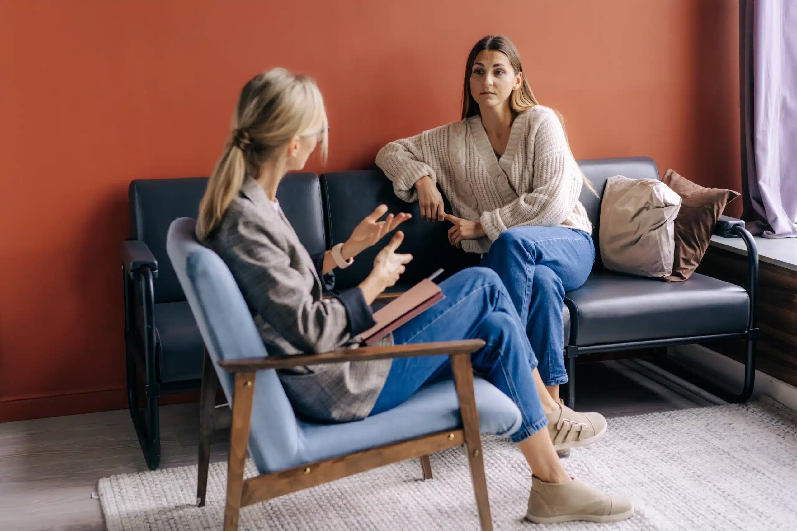 An ADHD coach facilitates a discussion with two clients on a sofa during a group coaching session in a comfortable office.