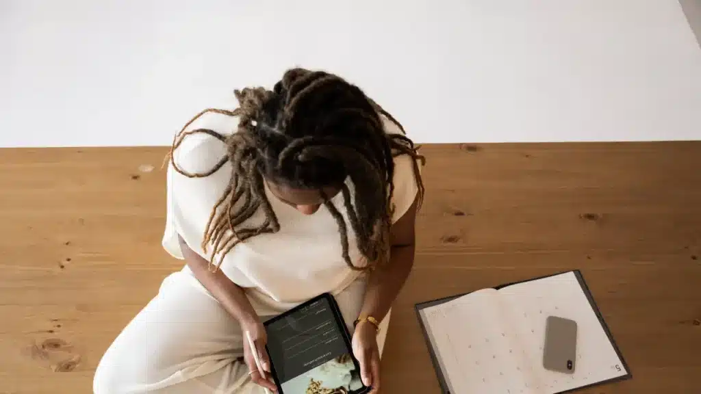 Overhead view of a woman using a paper planner and digital tablet simultaneously as effective adhd time management tools.